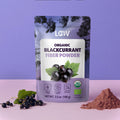 Packaging of LOOV organic blackcurrant fiber powder with berries and green leaves, next to a small mound of powder. Background is purple, conveying a natural, healthy vibe.