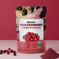 Packaging of LOOV Organic Wild Cranberry Fibre Powder against a pink background. Fresh cranberries and a pile of cranberry powder are beside it, conveying a natural and organic vibe.